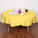 A table with a yellow Creative Converting Mimosa Yellow OctyRound tablecloth and plates and cups on it.