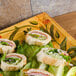 A Venetian tray with sandwiches on lettuce and a wood surface.
