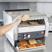 A person putting toast in a Hatco TQ-1800H conveyor toaster.