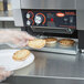 A person in gloves putting bread into a Hatco Conveyor Toaster.