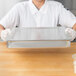 A woman wearing a white shirt using an American Metalcraft square deep dish pizza pan separator to hold food on a counter.