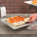 A hand taking a slice of pizza from an American Metalcraft square deep dish pizza pan.
