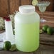 A Carlisle white container of green limeade with a lime wedge on a table.