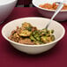 A tan SuperMel melamine bowl filled with beef and broccoli with a spoon in it.
