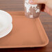 A hand holding a paper cup over a dark peach Cambro rectangular cafeteria tray.