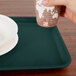 A hand holding a cup over a teal rectangular tray.