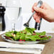 A hand holding a fork over a Carlisle Petal Mist clear plastic plate of salad.