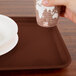A hand holding a paper cup over a brown rectangular Cambro tray.