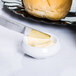 A knife spreading butter on a small white container with a Carlisle butter dish.