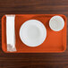 A rectangular orange Cambro tray with a bowl, cup, and napkin on it.