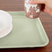 A hand holding a paper cup over a Cambro tray with a plate on it.