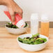 A hand squeezing Tablecraft Dualway Squeeze Bottle to pour pink liquid onto a bowl of salad.