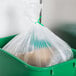 A green plastic bag twist tie securing a plastic bag in a green bin.