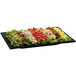 A black rectangular Tablecraft platter with a salad topped with lettuce, tomatoes, and other vegetables.