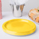 A stack of Creative Converting School Bus Yellow paper plates on a white background with a yellow plate next to a bucket of food.