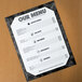 An 8 1/2" x 11" black menu with a white marble border on a table.