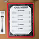 A black menu with a marble border on a table with silverware.