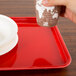 A hand holding a paper cup over a red rectangular Cambro tray.