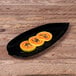 A black Elite Global Solutions leaf-shaped melamine platter with papaya slices on it.