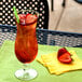 A Libbey Squall hurricane glass filled with red liquid and strawberries on a yellow napkin.