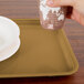 A hand holding a white cup over a brown Cambro cafeteria tray.