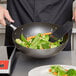 A person using a Vollrath SteelCoat Stir Fry Pan to cook vegetables.