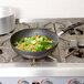 A Vollrath SteelCoat x3 Non-Stick Carbon Steel stir fry pan with vegetables cooking on a stove top.