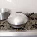 A silver Vollrath SteelCoat stir fry pan on a stove.