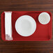 A red rectangular Cambro tray with a white cup and napkin on it.