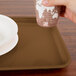 A hand holding a paper cup over a brown rectangular tray with a white bowl and a plate on it.