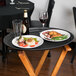 A Cambro black non-skid oval serving tray with food, a glass of red wine, and a plate of food on a table.