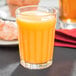 A Libbey paneled juice glass filled with orange juice on a table.