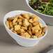 A white Elite Global Solutions melamine bowl filled with croutons on a table with a salad.