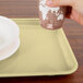 A hand holding a cup over a Cambro rectangular lemon chiffon tray with plates.