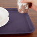 A hand holding a paper cup over a Cambro rectangular grape tray with plates and bowls.
