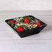 A black Elite Global Solutions square melamine bowl filled with salad and strawberries.