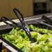 A black plastic salad with a pair of Fineline black plastic tongs.