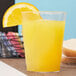 A Fineline clear hard plastic tumbler filled with orange juice with a slice of orange on top.