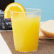 A clear plastic Fineline crystal tumbler filled with orange juice and a slice of orange on top.