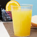 A clear Fineline plastic tumbler of orange juice with a yellow straw and a slice of orange.