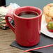 A red Tuxton Tiara mug on a table with a drink next to a muffin.