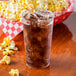 A Fineline clear hard plastic tumbler filled with soda and ice on a table with popcorn.