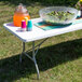 A white Flash Furniture folding table set up with a bowl of salad and a bowl of fruit on it.