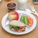 A Carlisle white melamine plate with a sandwich, apple, carrots, and celery.