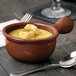 A Tablecraft maroon speckle cast aluminum soup bowl with a spoon and a fork on a table.