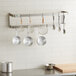 A kitchen with a Regency stainless steel wall mounted double line pot rack holding pots and pans.