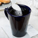 A spoon of sugar being poured into a cobalt blue CAC Venice Victory mug.