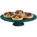 A Tablecraft hunter green cast aluminum cake stand with fruit on it.