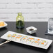 A rectangular white Tuxton china plate with a sushi roll on it and chopsticks.