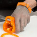 A hand wearing a Victorinox chain mail glove peeling an orange bell pepper.